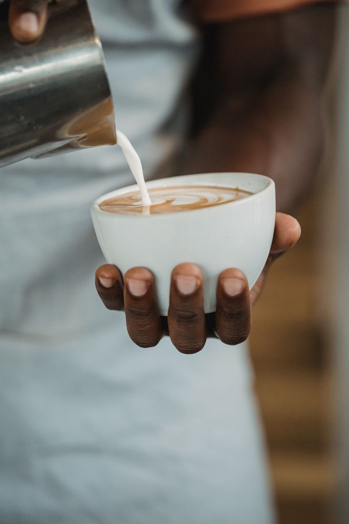 Close-up of barista crafting latte art with milk in a café setting.