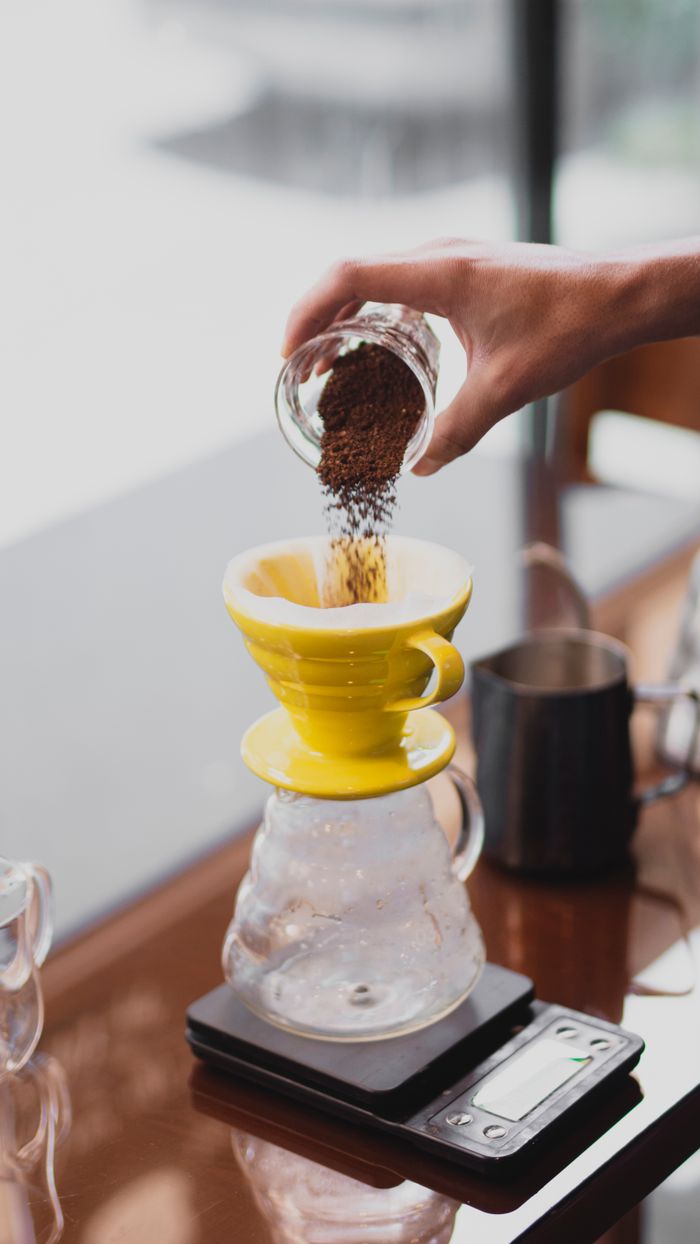 A hand pouring coffee grounds into a yellow dripper for manual coffee brewing.