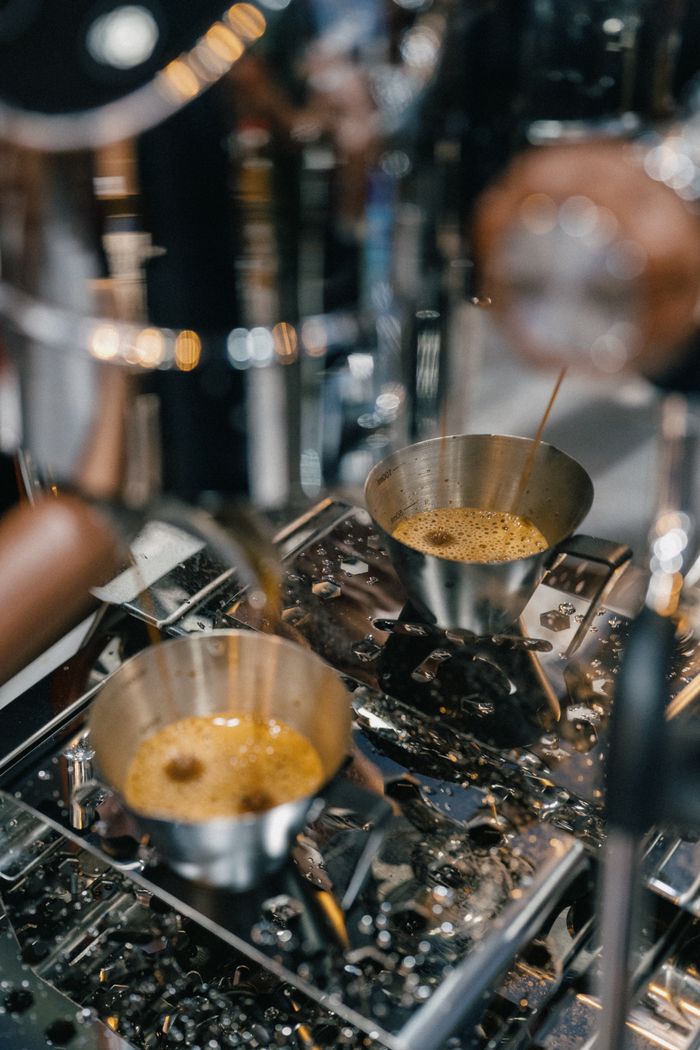 Close-up of espresso brewing in a coffee machine with metal cups capturing fresh coffee.