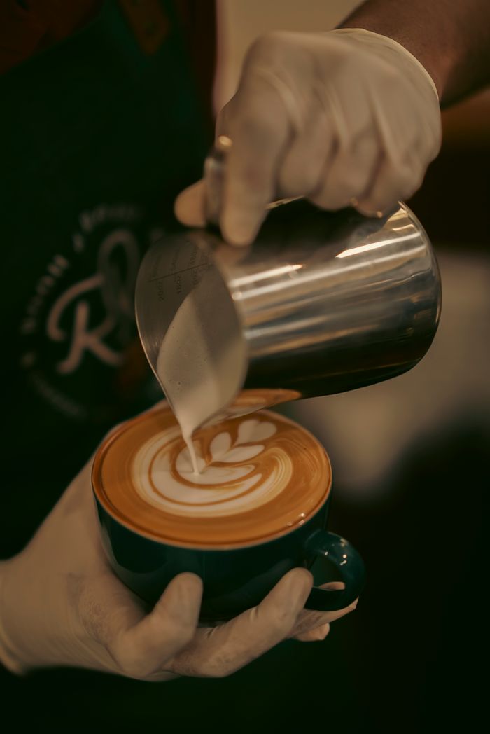 Barista pouring intricate latte art into a cup of coffee in a cozy cafe setting.