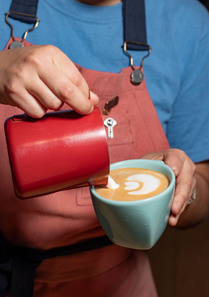 Barista creating intricate latte art with a milk frother in a cozy cafe setting.