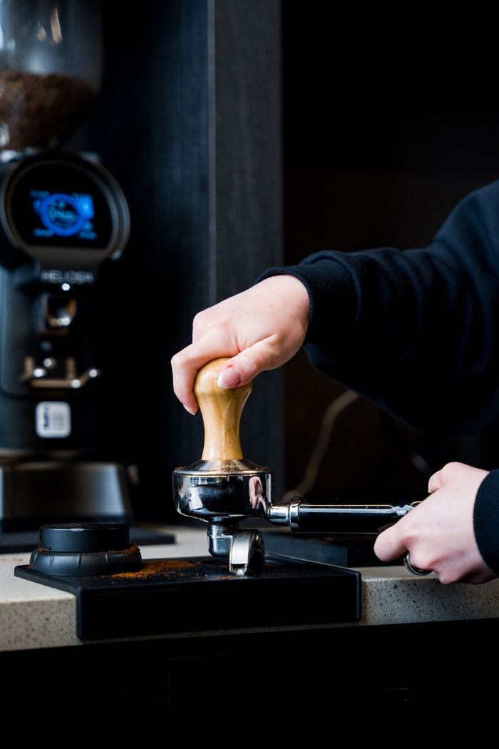 A barista tamping coffee grounds with a portafilter in a modern cafe setting.