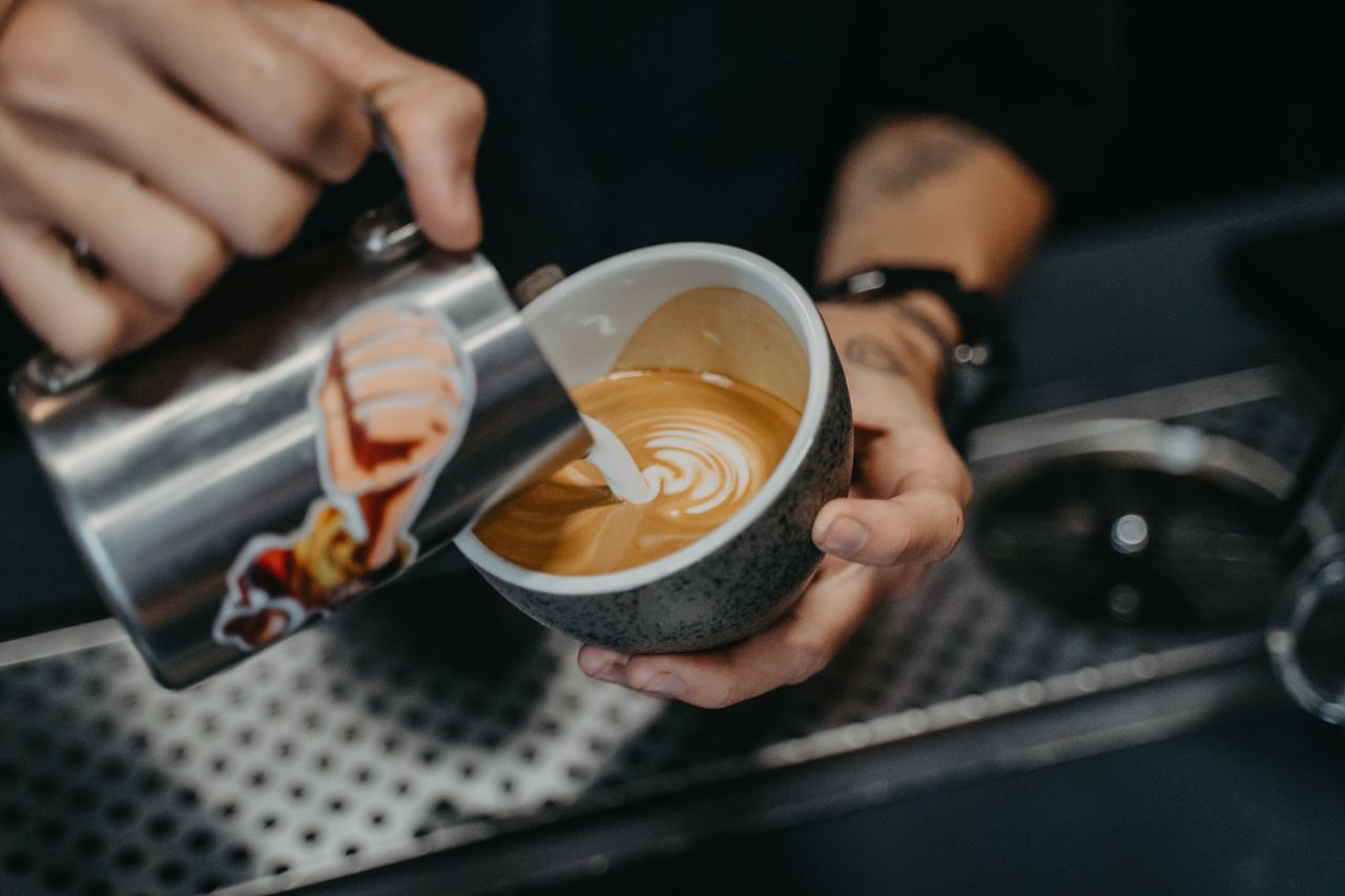 A barista skillfully pours latte art in a ceramic cup, showcasing precision and creativity.